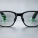 Black AI glasses with green in-lens displays showing navigation directions, messages, and information icons.
